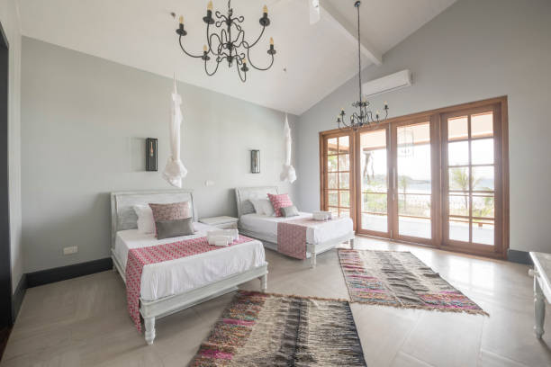 Modern hotel room with two beds and french doors with natural light, ethnic floor covering on tiled floor